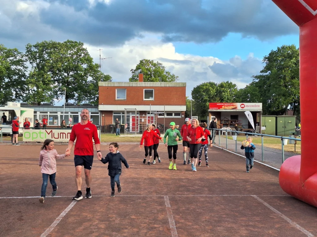 Laufveranstaltung: Familien und Sportler auf einer Aschenbahn bei bewölktem Himmel, Startbogen im Hintergrund.