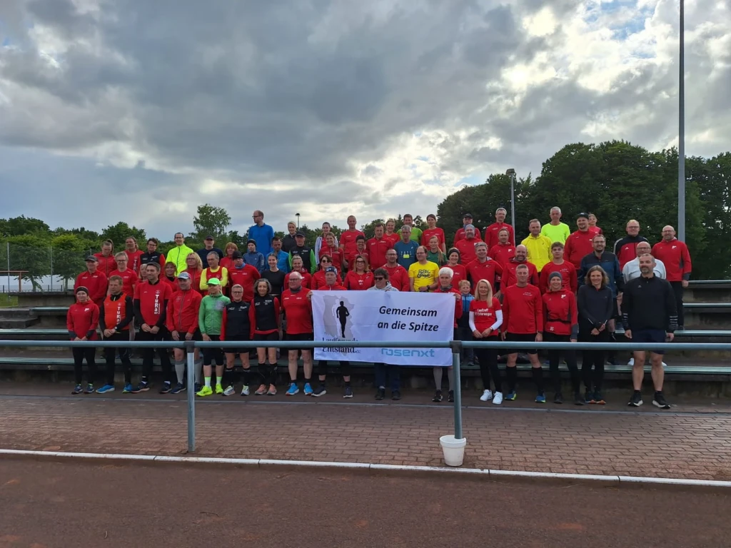 Gruppe von Menschen in Sportkleidung versammelt im Freien mit Banner Gemeinsam an die Spitze, bewölkter Himmel.
